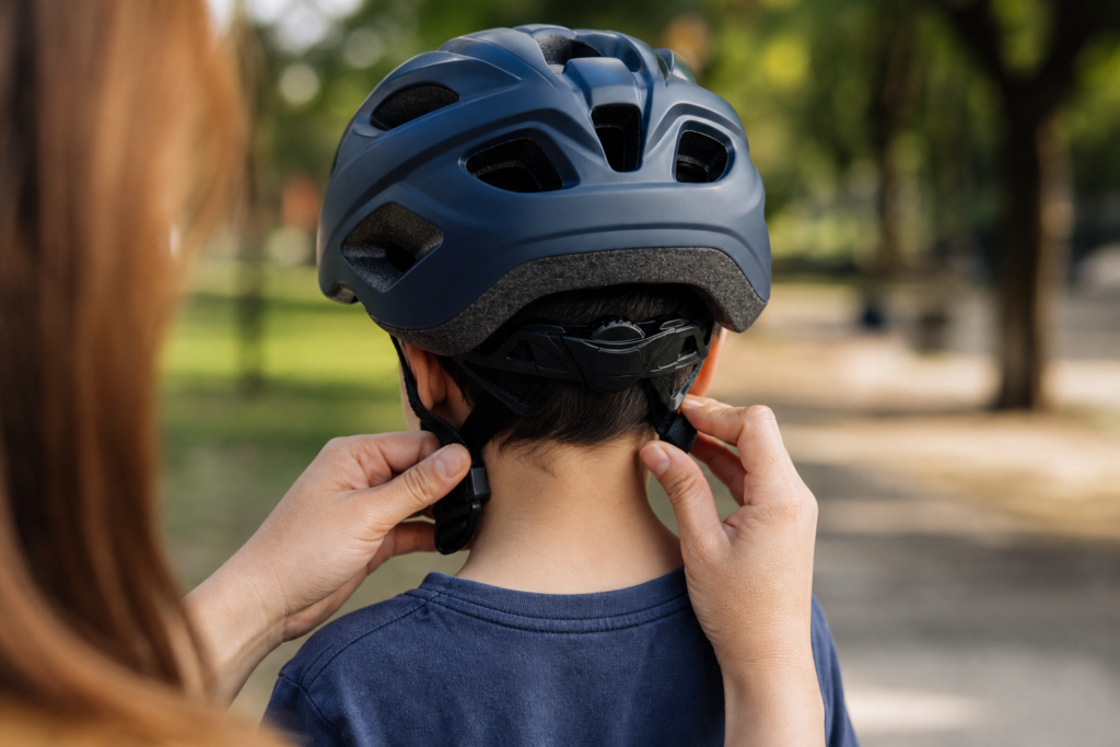 Cuidador ajustando capacete de bicicleta em uma criança para prevenir pancadas na cabeça